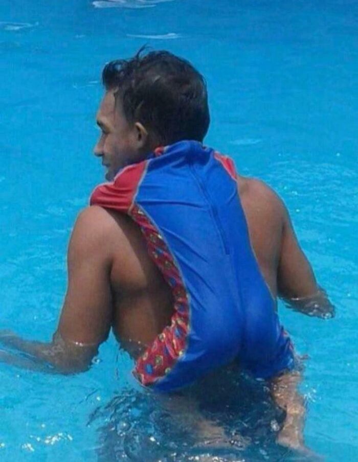 A man in a swimming pool with a child's swimsuit on his back, creating an optical illusion.