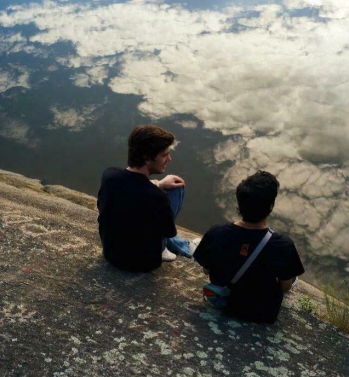 Two men sitting on a rock, looking at water that reflects the sky perfectly, an optical illusion.