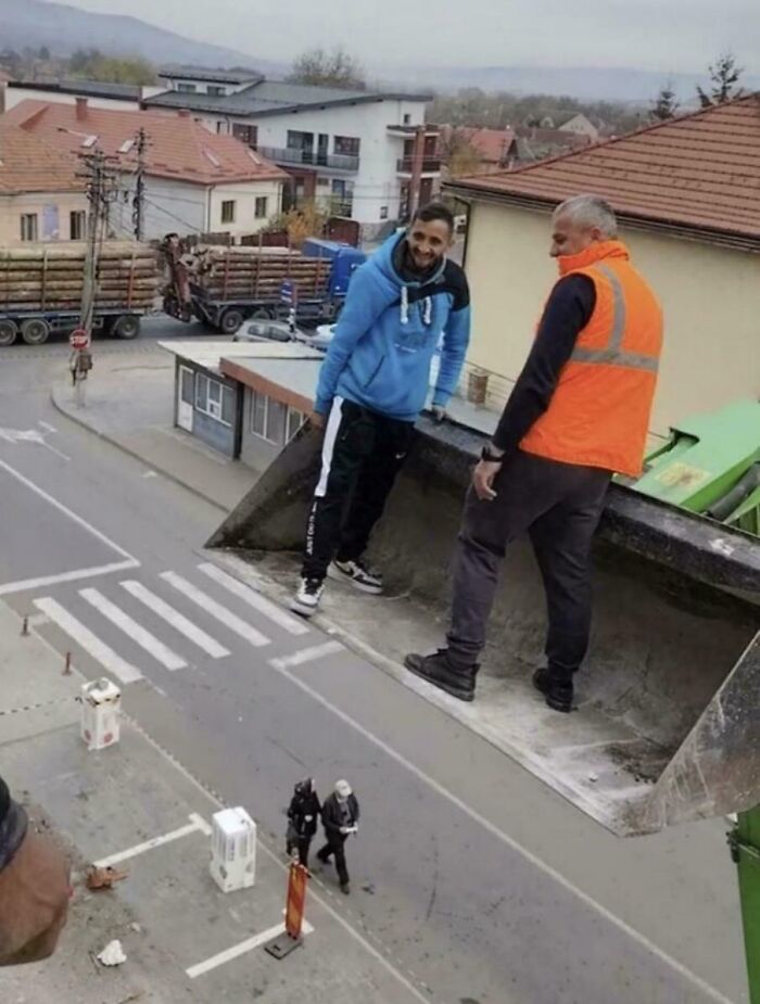 An optical illusion showing two men on a large shovel appearing to be giants over a town.