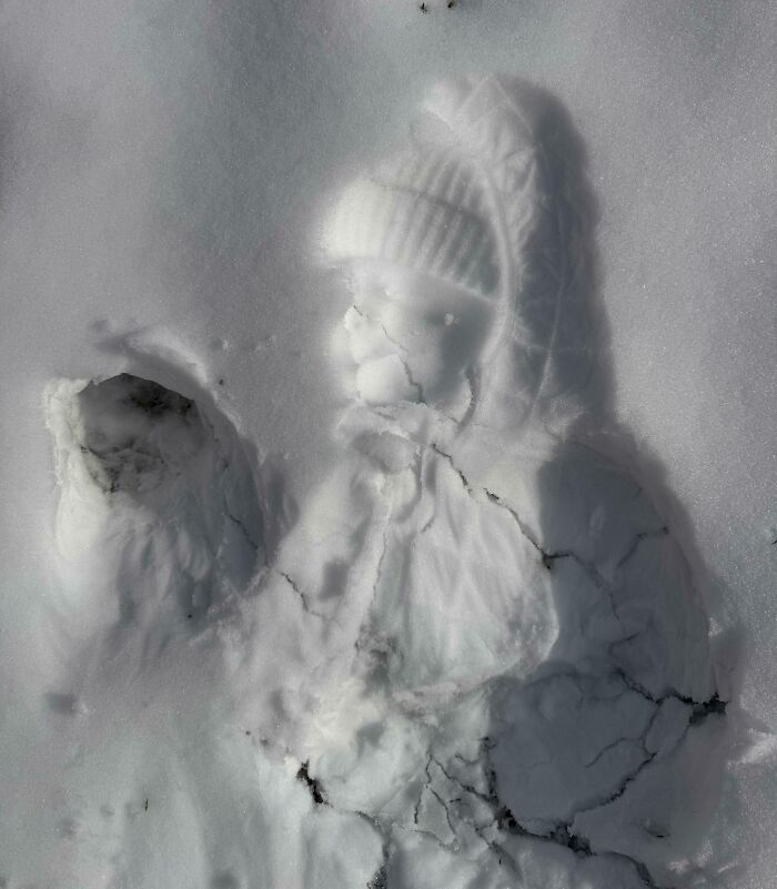 A detailed snow impression of a person wearing a hat and coat creates an amazing optical illusion in the snow.