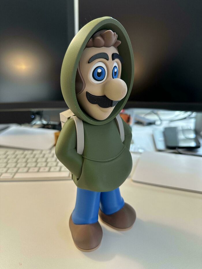 A cool 3D printed Luigi figurine in a green hoodie stands on a desk, a creative example of 3D printer projects.