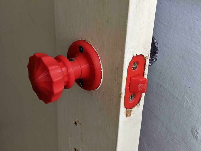 A red geometric 3D printed doorknob and latch installed on a white door, demonstrating unique projects.