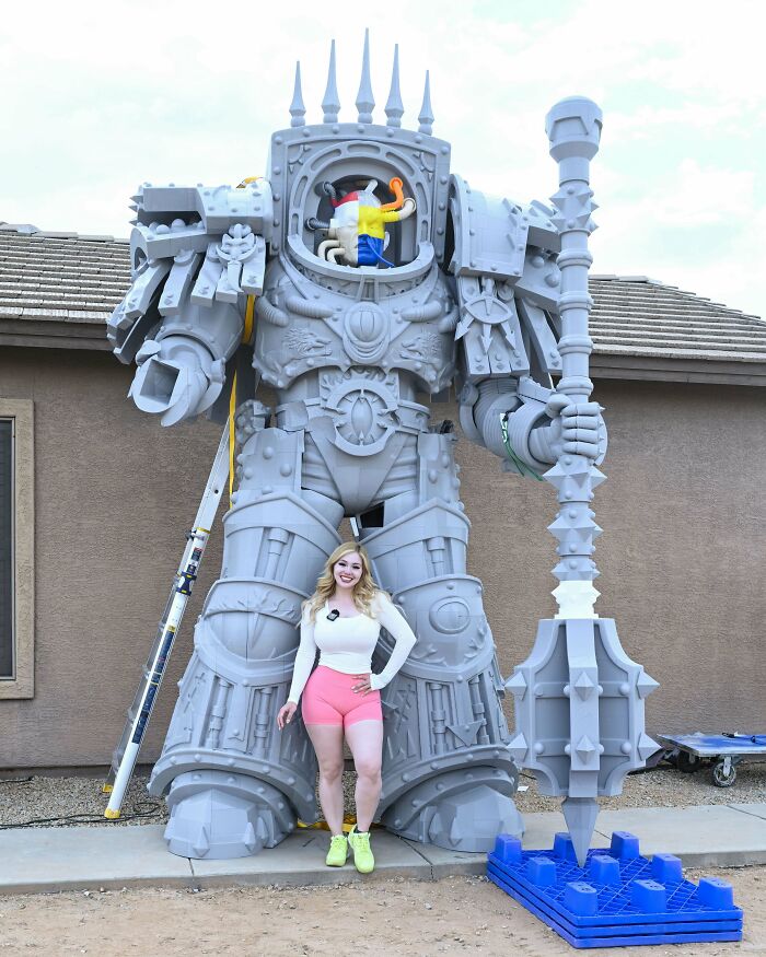 A woman stands beside a massive 3D printer statue of a robot, demonstrating cool 3D projects.