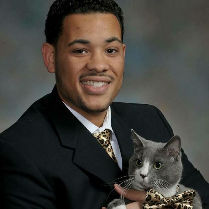 A man in a suit smiles while holding a gray cat with a matching bowtie, among the funniest animal photos.