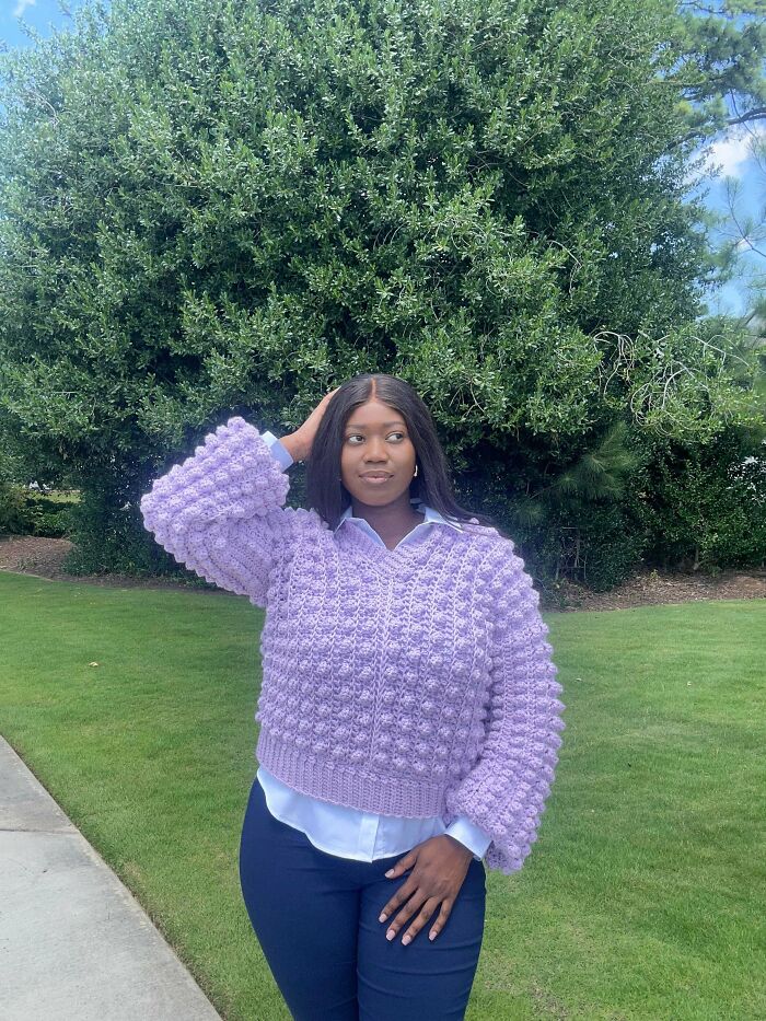 A woman poses outdoors, confidently wearing a stylish lavender crochet sweater with textured bobbles, highlighting incredible crochet fashion.