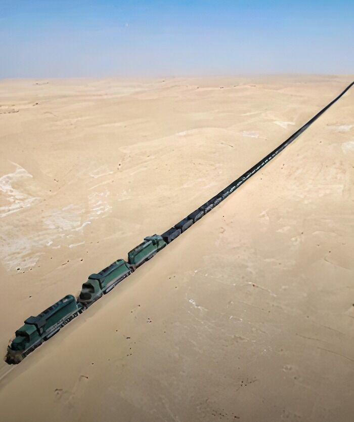 An extremely long train stretches across a vast, flat desert landscape, making it seem eerie and desolate.