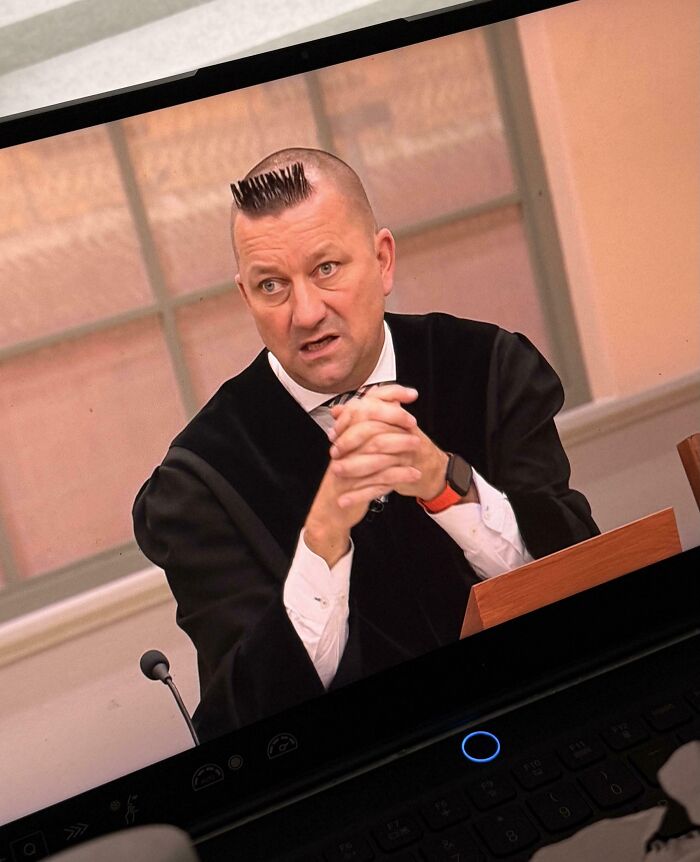 A man in a robe with a very short, spiky haircut, a clear bad hair mistake, on a screen.
