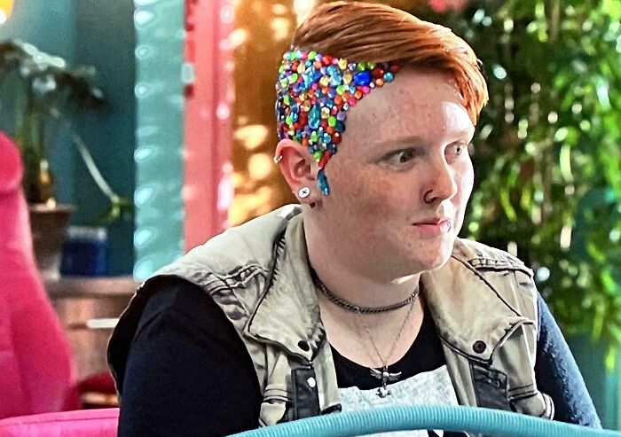 A person with bright red hair and a shaved side adorned with colorful jewels, showcasing a unique hair mistake.