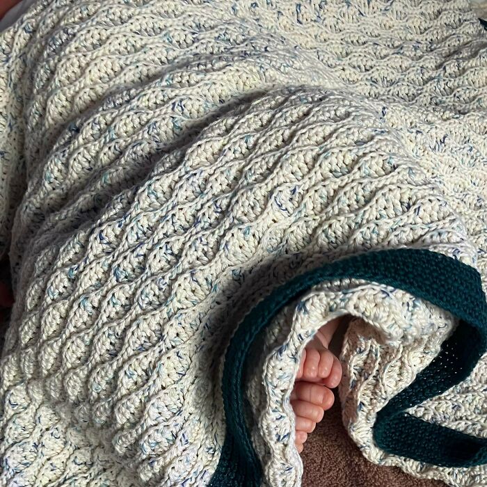A baby's feet peek out from under a soft, white and blue crochet blanket, showcasing incredible crochet artistry.