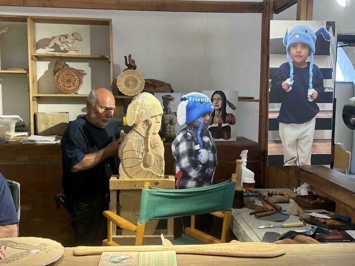 A man carving wood, with a small child next to him wearing a blue hat, demonstrating chaotic good posts in real life.
