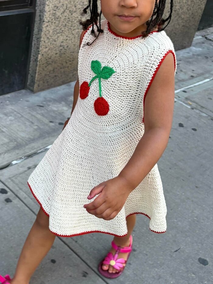 Child wearing a handmade crochet dress with cherry design in yarn