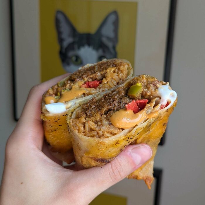 A hand holding a burrito cut in half, representing the consumerism culture and food prices.