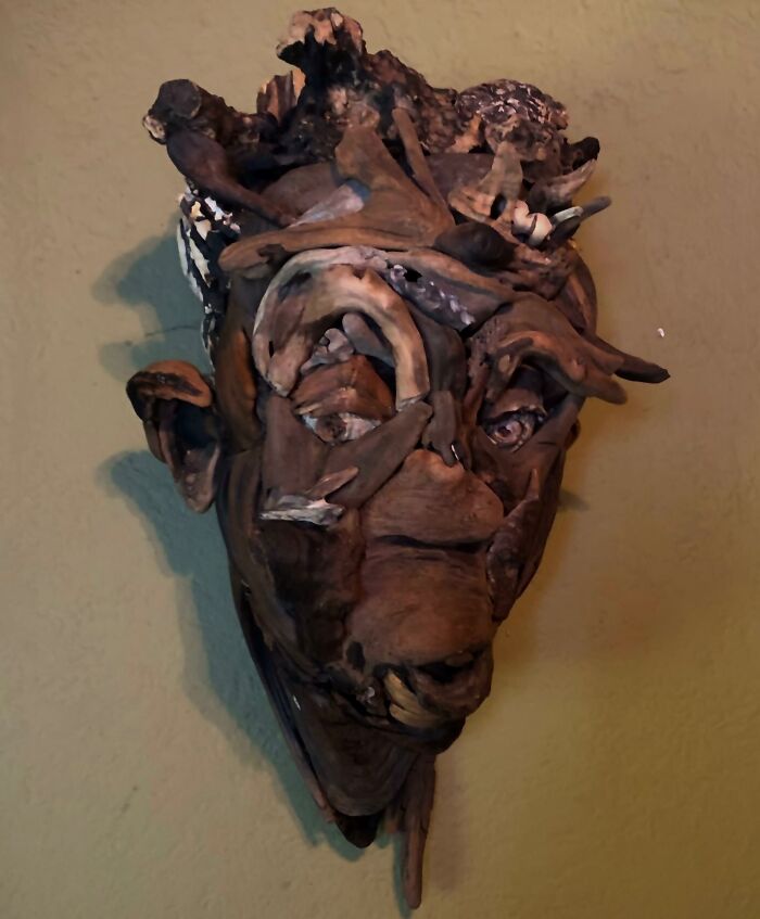 A stunning sculpture of a man's face crafted from various collected pieces of wood, with a textured background.