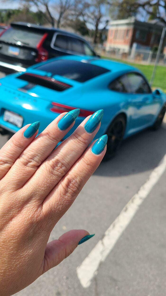 A hand with teal nails perfectly matching a teal sports car in the background. A satisfying paint match.