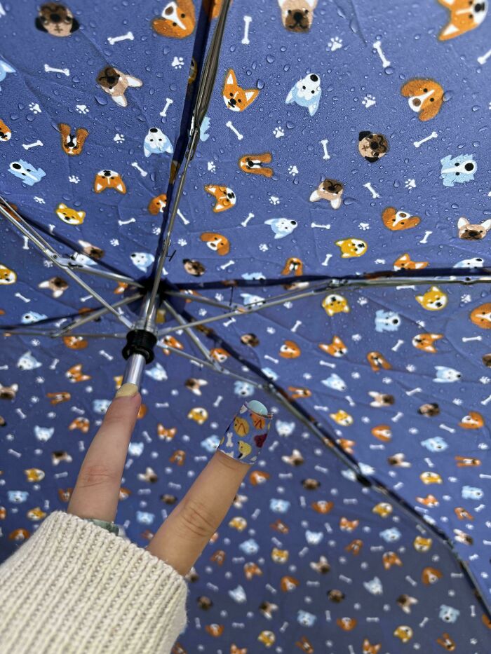 A hand holding up a blue umbrella with puppy and bone designs, perfectly matching the nail art. Satisfying paint matches.