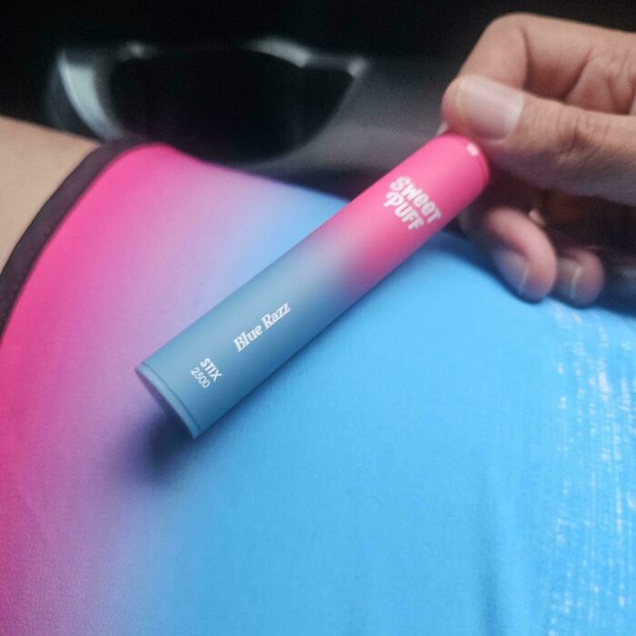 A hand holds a pink and blue vape that perfectly matches the pink and blue shirt below, a satisfying paint match.