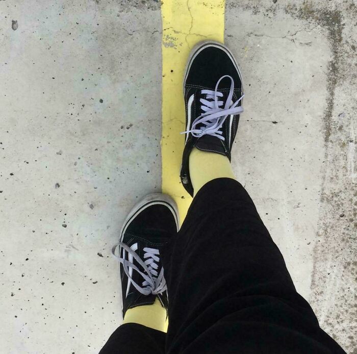 A person with black sneakers and yellow socks stands on a yellow line, creating a satisfying paint match.