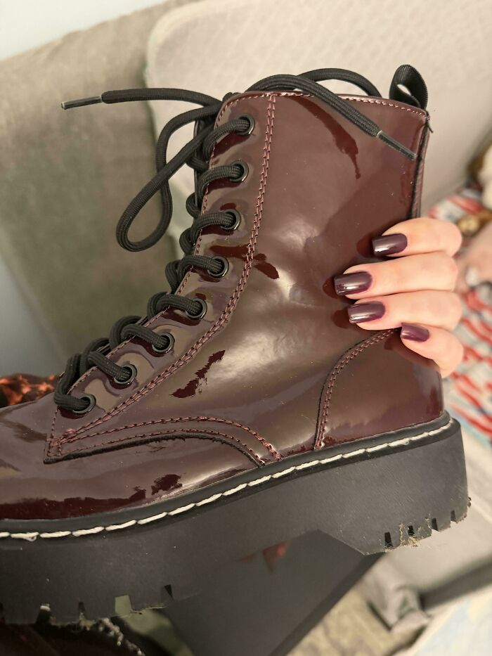 A person's hand with dark purple nail polish holding a shiny dark red boot, showcasing satisfying paint matches.