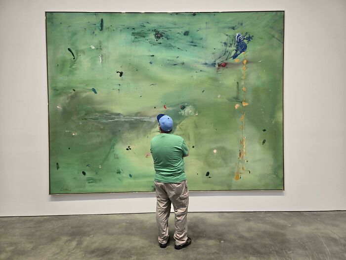 A man in a blue hat looking at a large green abstract painting, showcasing satisfying paint matches.