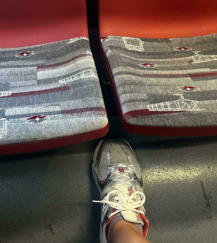 A person's foot in a grey and red sneaker on a grey floor, perfectly matching the patterned fabric of train seats, showcasing satisfying paint matches.