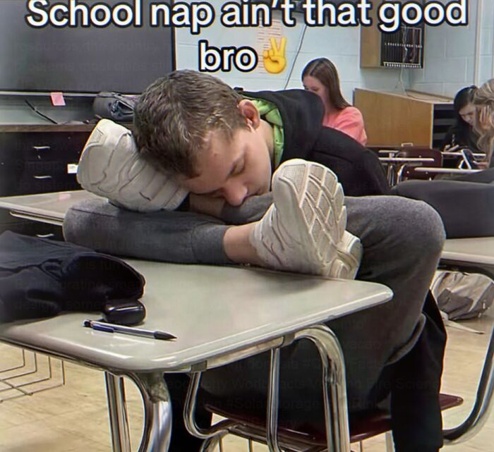 A student awkwardly sleeping on a school desk, head on arm and feet on the desk, highlighting weird memes about school.