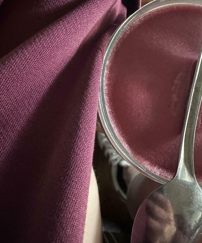 A perfect paint match between a person's maroon sweater and a dessert in a clear cup with a spoon.