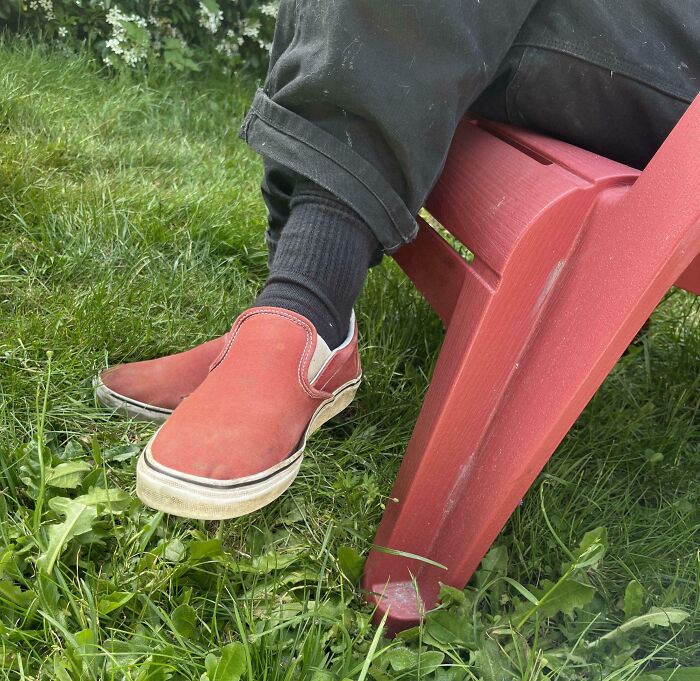 A person wearing red slip-on shoes and black socks, sitting on a red chair, showing a perfect paint match.
