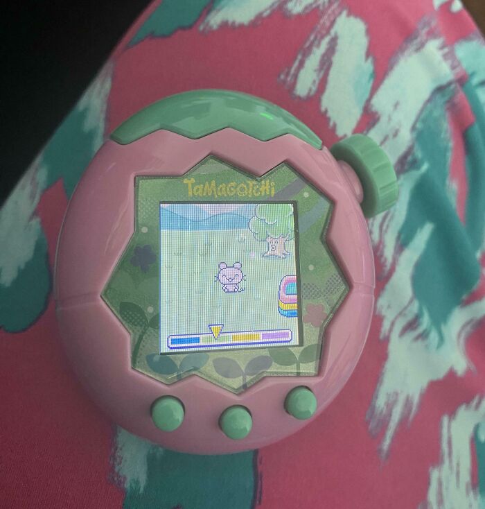 A pink and green Tamagotchi device on a colorful patterned fabric, creating a satisfying paint match.