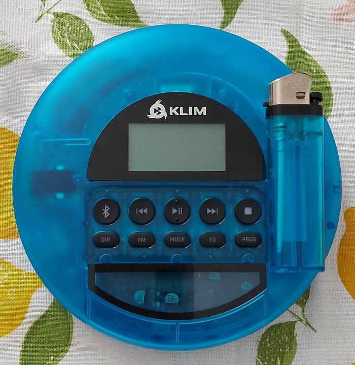 A blue KLIM portable music player and a clear blue lighter on a lemon-patterned fabric, showing a satisfying paint match.
