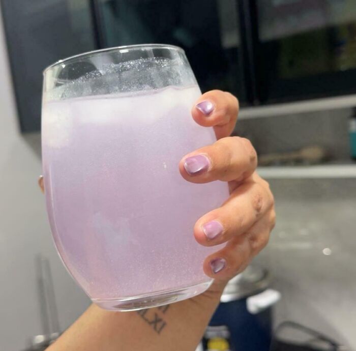 A hand holding a glass of light purple liquid with ice, featuring light purple painted nails, a perfect paint match.