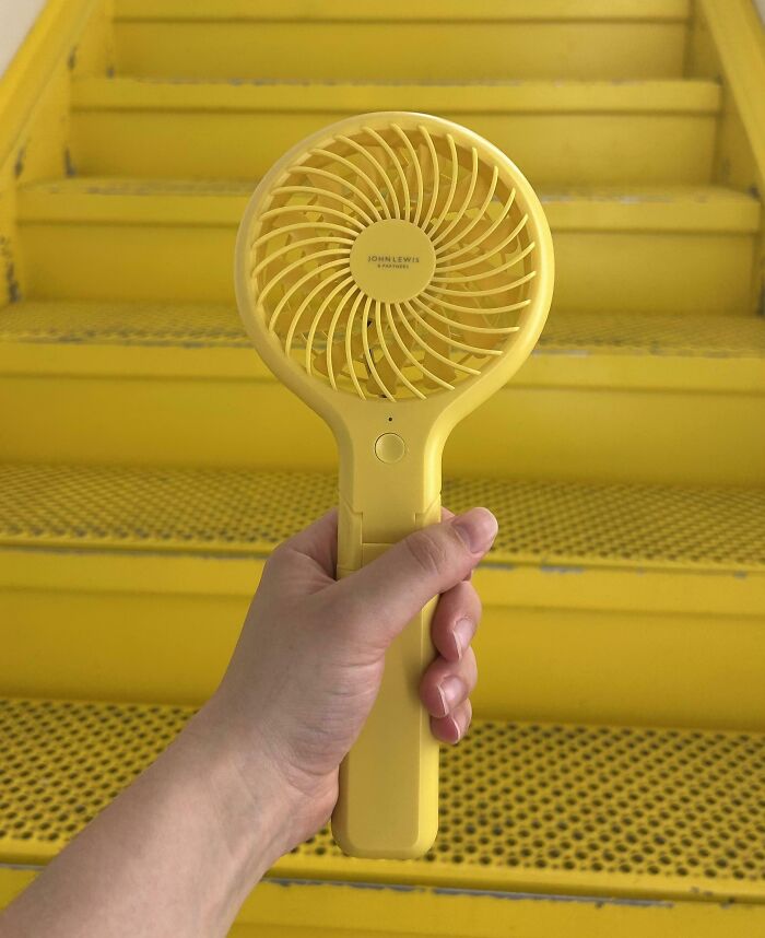 A hand holding a yellow portable fan against a bright yellow staircase, an incredibly satisfying paint match.