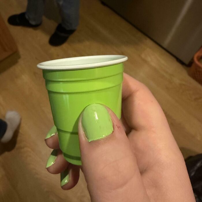 A person's fingers with light green nail polish hold a small green plastic cup, the nail color a perfect match for the cup, showcasing satisfying paint matches.