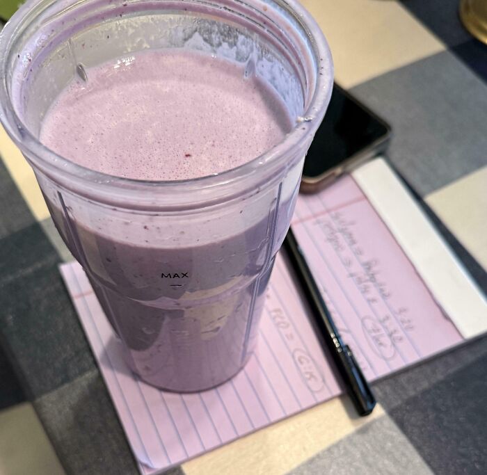 A purple smoothie in a clear glass sits on a pink notepad, perfectly matching the smoothie's color, a satisfying paint match.