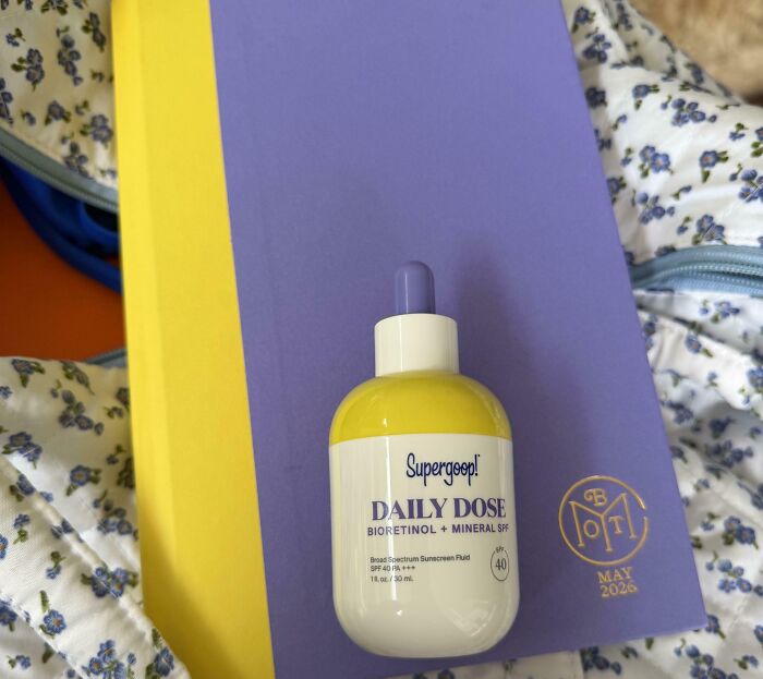 A yellow and purple bottle of Supergoop sunscreen sits on a matching yellow and purple book, a satisfying paint match.