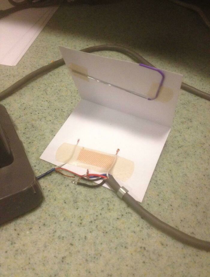 A bandage and paperclip used to hold together frayed wires, an unhinged way to fix something with household items.