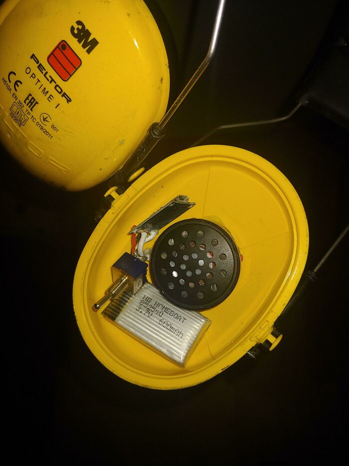 A yellow ear defender with its cover removed, showing internal wiring, a battery, and a speaker, a wild way to fix it.