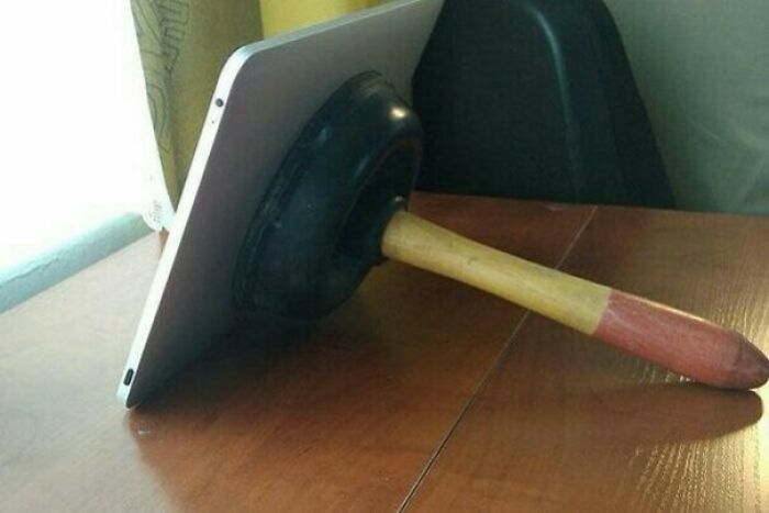 A tablet held upright by a plunger suctioned to its back, a wild and unhinged way to fix a stand.