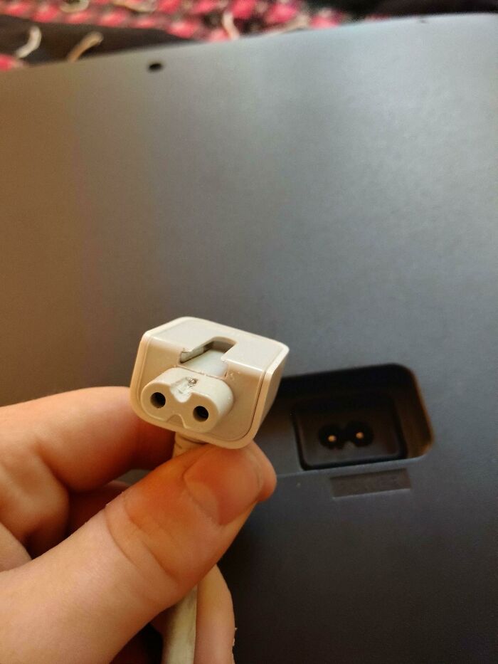 A hand holds a broken laptop charger, a wild way to fix something.