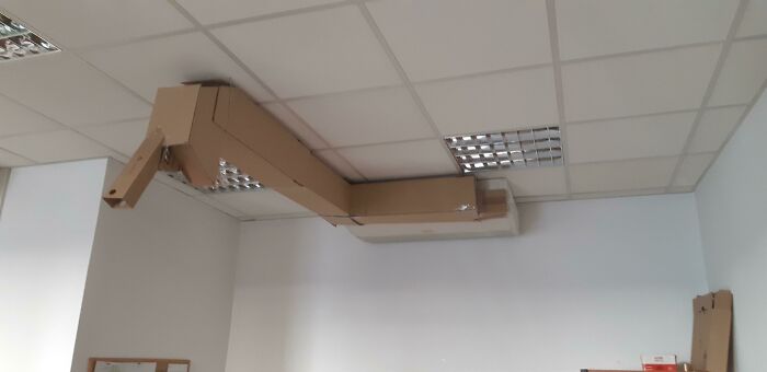 A wild and unhinged way to fix an air conditioner, using a cardboard duct extension on a ceiling.