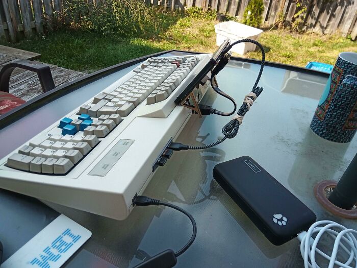A wild and unhinged way to fix an old keyboard, powered by a modern power bank on a glass table outdoors.