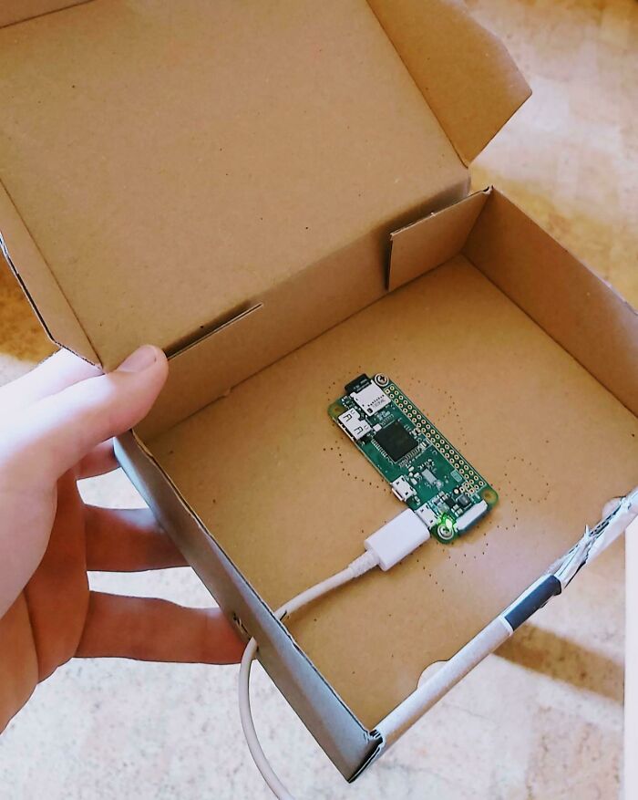A hand holds a cardboard box with an unhinged small circuit board and charging cable inside, a wild fix.
