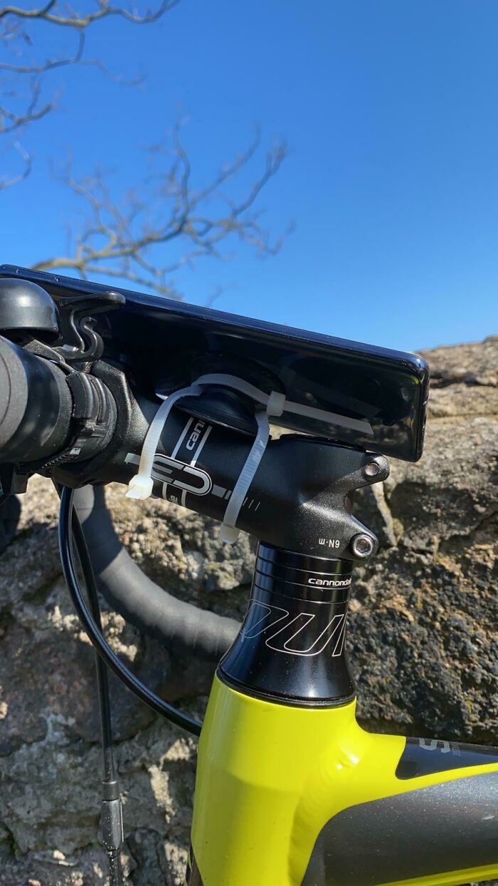 A smartphone attached to a bicycle handlebar with a cable tie, showcasing an unhinged way to fix it.