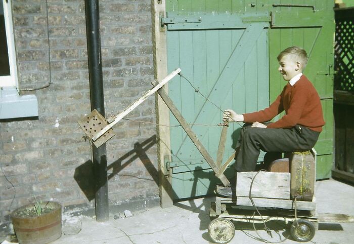 A young boy sitting in a homemade, unhinged wooden contraption with wheels, a wild way to fix playtime.