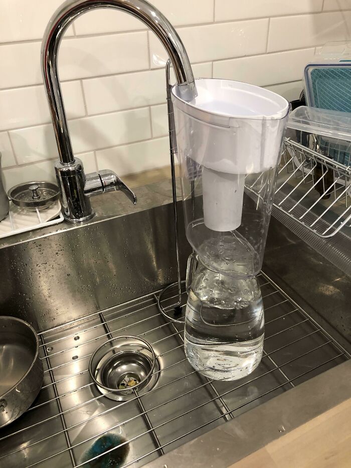 A water filter pitcher precariously propped to fill from a sink faucet, illustrating unhinged ways to fix something.