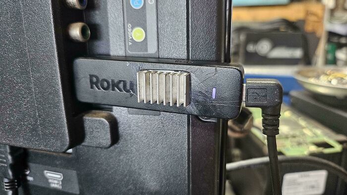 A Roku streaming stick fixed on a TV with unhinged ways to fix something with tape.