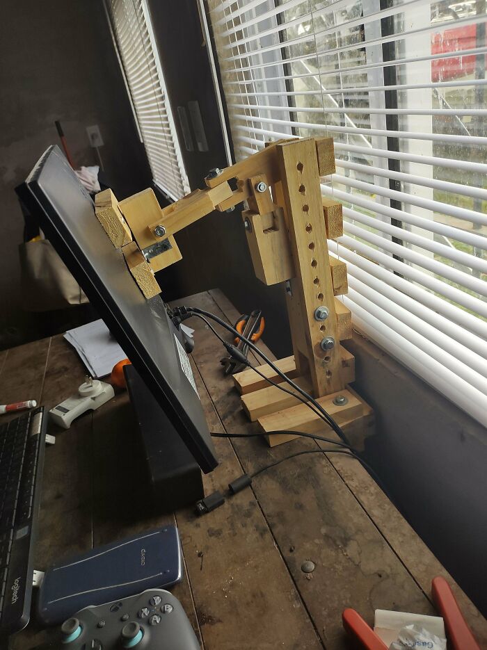 A monitor attached to a wooden, unhinged stand, demonstrating a wild way to fix something.