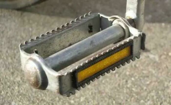 A close-up of a classic metal bicycle pedal with a yellow reflector, a common sight in the 80s.