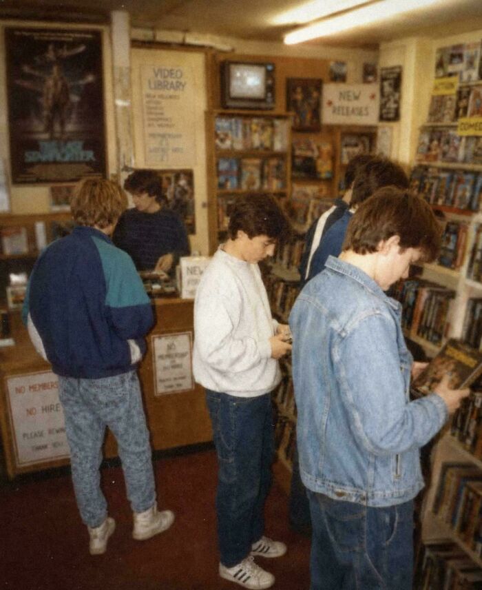 Young men in a video rental store in the 80s, looking through VHS tapes and bringing back good memories.