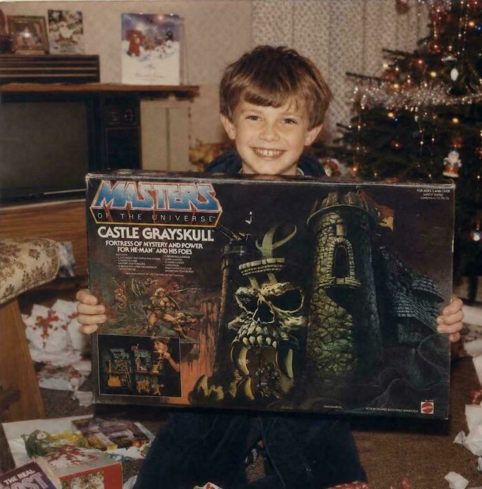A happy young boy in the 80s holding a Masters of the Universe Castle Grayskull toy for Christmas.