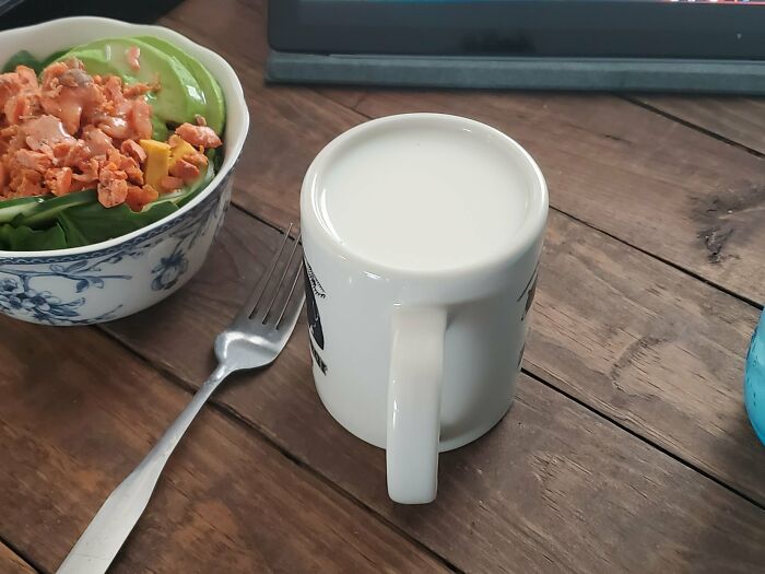 A close-up shot of a white mug filled with milk, next to a bowl of salad, showing a photo that may need a second look.